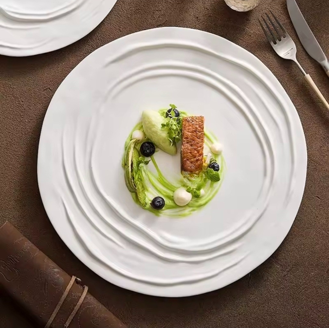 Ripple-edge porcelain dinner plates in 26cm and 31cm sizes, styled with elegant food plating on a brown linen tablecloth.