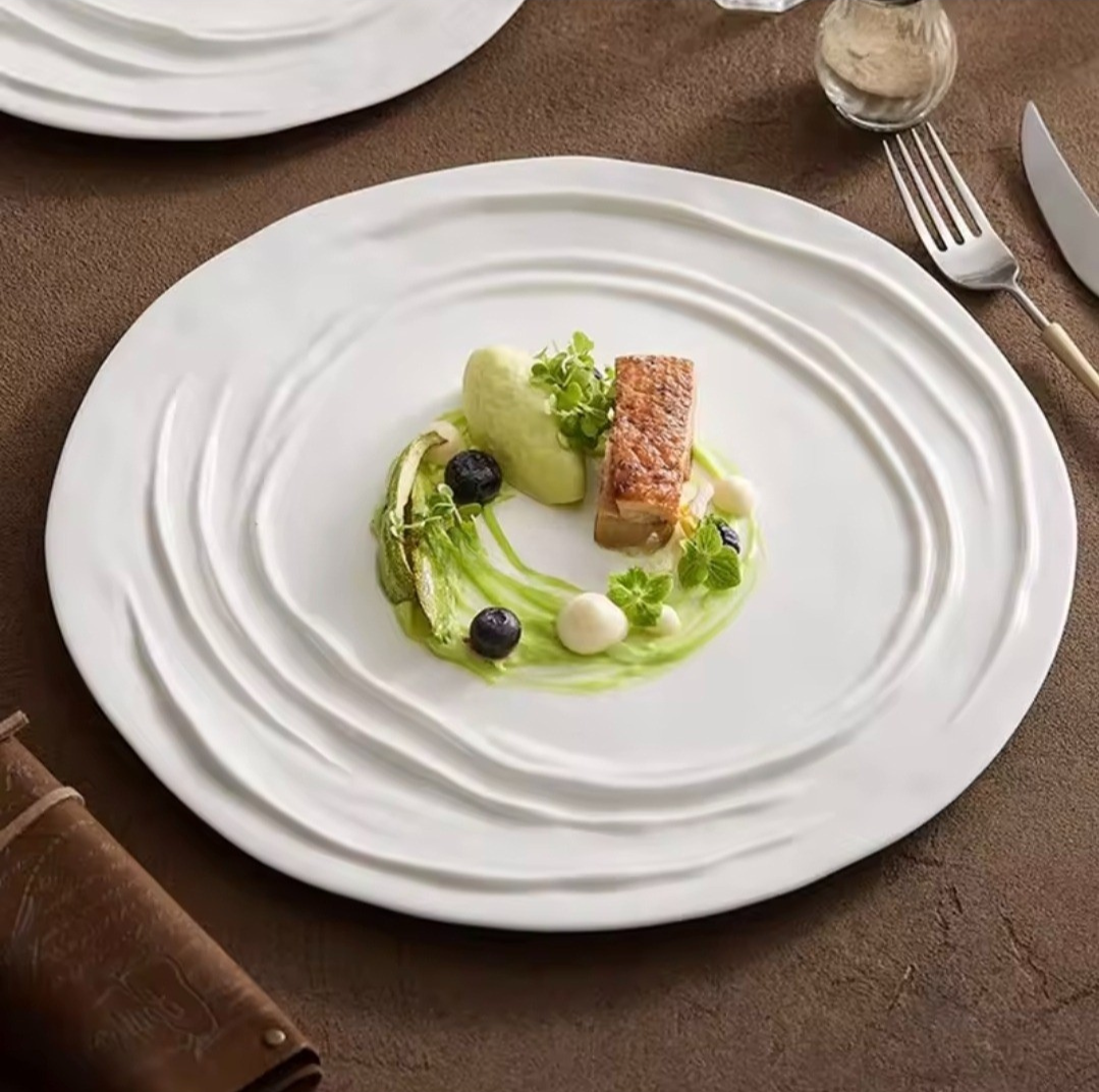 Ripple-edge porcelain dinner plates in 26cm and 31cm sizes, styled with elegant food plating on a brown linen tablecloth.